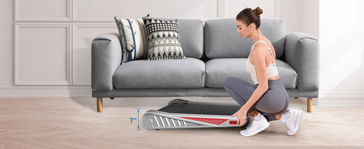 Woman using a portable treadmill in a living room with a gray sofa and wooden floor.